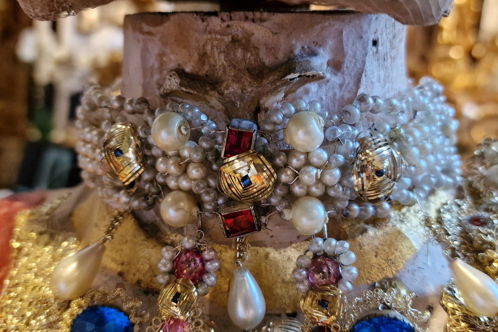 Der aufwendige Halsschmuck mit Perlen und roten Steinen ist um den Hals des Katakombenheiligen gebunden. Tomedi Textilrestaurierung